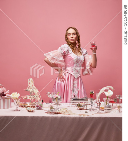 Shot of beautiful woman, princess wearing renaissance pink dress and standing with wine glass over studio background. Serious, arrogant queen Shot of beautiful woman, princess wearing renaissance pink dress and standing with wine glass over studio background. Serious, arrogant queen 101548099