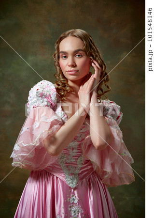 Shot of beautiful woman wearing vintage pink dress and standing with folded hands over vintage texture background. Medieval charming queen 101548146