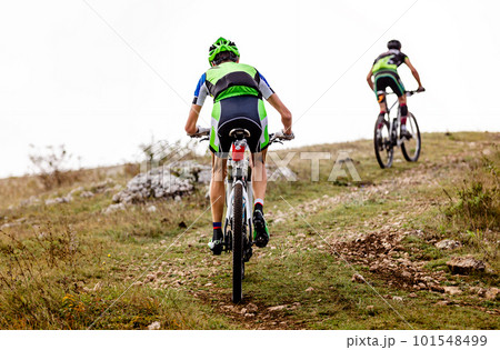 rear view two male mountainbiker riding together sports cycle on mountainous trail in cross-country cycling race 101548499