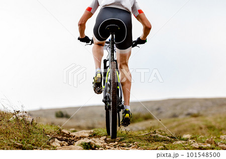 rear view male mountainbiker riding sports cycle on mountainous trail in cross-country cycling race 101548500