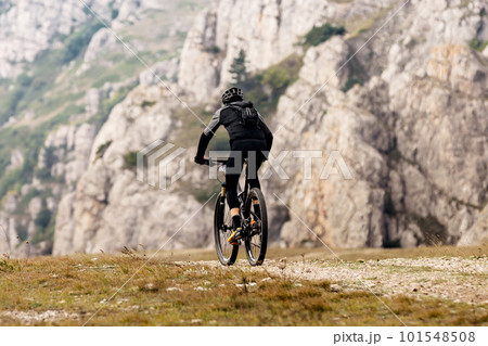 male cyclist riding mountain bicycle on mountainous region travelling cycling. backpack on back of mountain biker 101548508