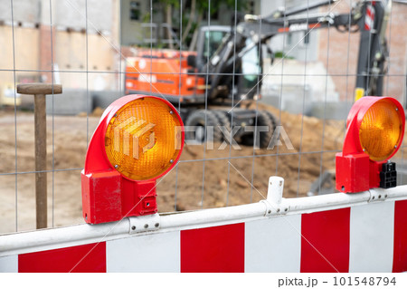 Close-up detail view orange flasher safety blinker light barrier against fence construction site work area. Security equipmnent barricade fuse lamp city street building construction machinery traffic Close-up detail view orange flasher safety blinker light barrier against fence construction site work area. Security equipmnent barricade fuse lamp city street building construction machinery traffic 101548794