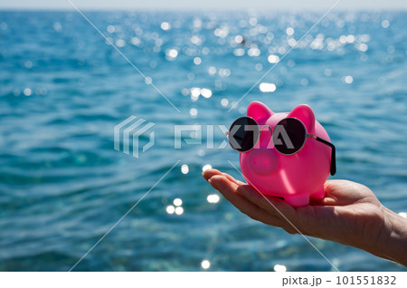 A woman holds a piggy bank in sunglasses on the background of the sea. Budget vacation. 101551832