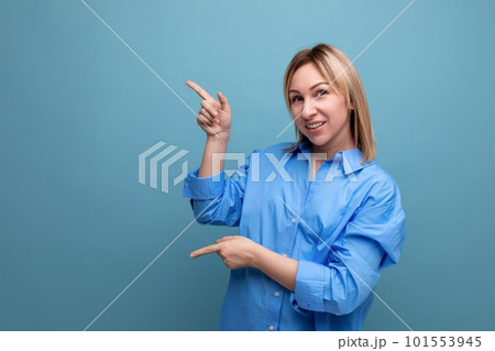european blond young woman in a casual shirt shows her hands to the left at a baner on a blue 101553945