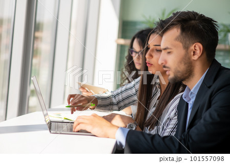 Creative business team sharing laptop in office, watching startup presentation, brainstorming, pointing at monitor, talking. 101557098