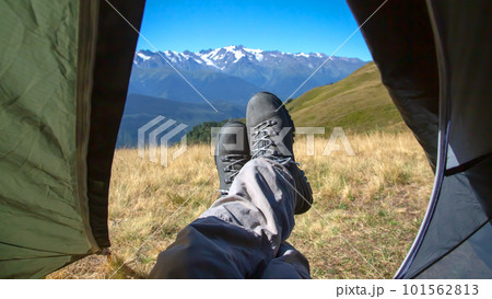 leg tourist in boots out of the tent with mountains in the background 101562813