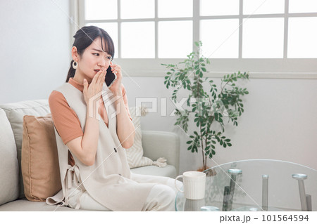 スマホで電話・通話・会話しながら驚く・びっくりするソファに座ったアジア人女性 101564594