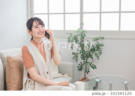 ソファに座ってスマホで友達と電話する笑顔のアジア人女性 ソファに座ってスマホで友達と電話する笑顔のアジア人女性 101565120