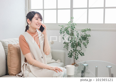 ソファに座ってスマホで友達と電話する笑顔のアジア人女性 ソファに座ってスマホで友達と電話する笑顔のアジア人女性 101565121