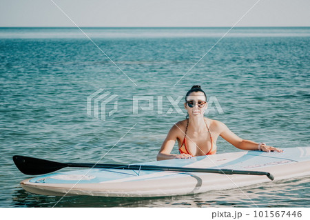 Sea woman sup. Silhouette of happy middle aged tanned woman in rainbow bikini, surfing on SUP board, confident paddling through water surface. Idyllic sunset. Active lifestyle at sea or river. 101567446