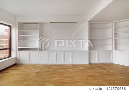 Empty built-in white cabinet on wooden laminate floor with big window in empty bright airy room in housewarming. Concept of housewarming and convenient storage Empty built-in white cabinet on wooden laminate floor with big window in empty bright airy room in housewarming. Concept of housewarming and convenient storage 101570638