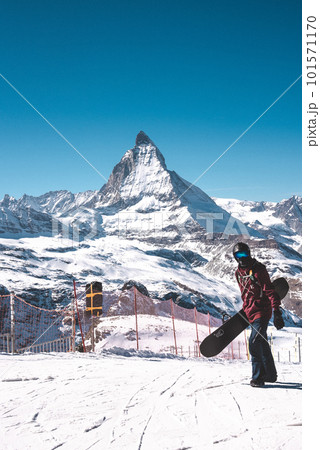 Young snowboarder spending winter holidays in Zermatt, near the famous Matterhorn peak. Male posing in Swiss Alps for the snowboarding season. Young snowboarder spending winter holidays in Zermatt, near the famous Matterhorn peak. Male posing in Swiss Alps for the snowboarding season. 101571170