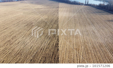 Half of large field after wheat harvest, half of field plowed. Flying over field with dry straw from wheat and brown dug up earth. Natural agricultural background. natural farming industrial backdrop. 101571206