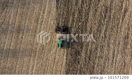 Tractor plowing the ground. Flying over green tractor that plows up ground in yellow field after harvesting wheat on autumn day. Agricultural work on field. Tractor digging land. Aerial drone view Tractor plowing the ground. Flying over green tractor that plows up ground in yellow field after harvesting wheat on autumn day. Agricultural work on field. Tractor digging land. Aerial drone view 101571209