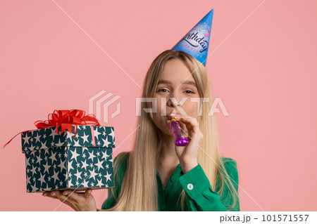 Happy excited lucky woman wearing birthday hat cone blow pipe celebrating party success win victory Happy excited lucky woman wearing birthday hat cone blow pipe celebrating party success win victory 101571557