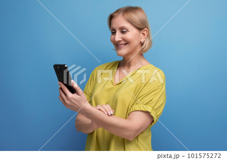 pleasant blond middle-aged woman holding a gadget phone in her hands vertically 101575272