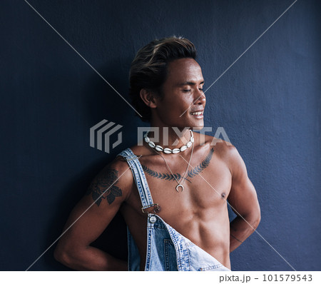 Smiling guy with closed eyes leaning against a blue wall. Stylish male wearing overall with bare chest relaxing outdoors.	 101579543