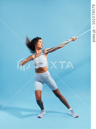 Full length of a slim woman in sportswear practicing on blue background with a resistance band Full length of a slim woman in sportswear practicing on blue background with a resistance band 101579579