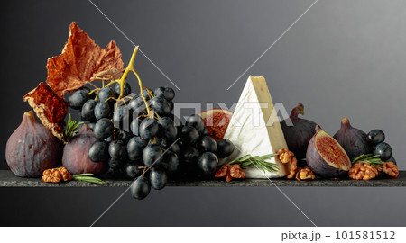 Cheese brie with figs, walnuts, and blue grapes on a dark background. 101581512