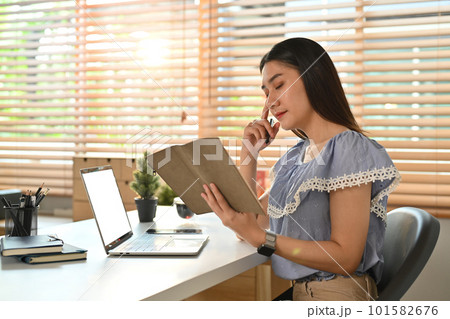 Serious young asian female entrepreneur reading notes in planner or checking her working schedule plan at workplace Serious young asian female entrepreneur reading notes in planner or checking her working schedule plan at workplace 101582676