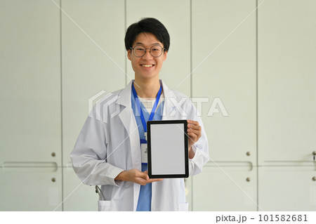 Doctor wearing white uniform showing digital tablet with blank screen for advertisement. Telehealth online applications concept 101582681