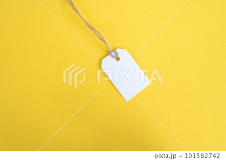 White tag with a thread on a yellow background. White price tag label mockup. Place to copy. 101582742