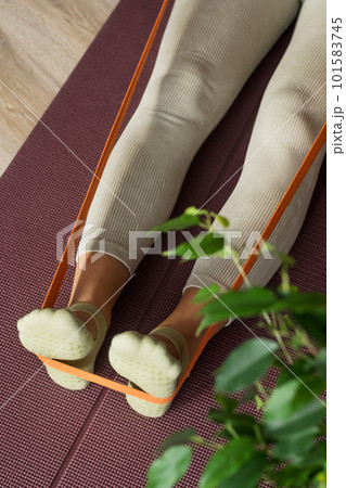 Trainer doing leg stretching exercises with orange fitness rubber bands. Fitness trainer doing exercises in pilates yoga studio. Concept of beauty, body care, health. Women health club 101583745