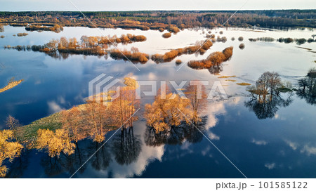 Spring flood rural landscape. Trees, meadow, bushes, fields, country road under High Water inundation. Sky and clouds reflection in evening light. Freshet Overflow aerial view. Spring flood rural landscape. Trees, meadow, bushes, fields, country road under High Water inundation. Sky and clouds reflection in evening light. Freshet Overflow aerial view. 101585122