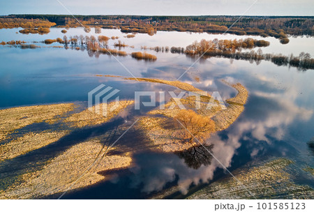 Spring flood rural landscape. Trees, meadow, bushes, fields, country road under High Water inundation. Sky, clouds reflection in evening light. Freshet Overflow aerial view. Floodplain area. Spring flood rural landscape. Trees, meadow, bushes, fields, country road under High Water inundation. Sky, clouds reflection in evening light. Freshet Overflow aerial view. Floodplain area. 101585123