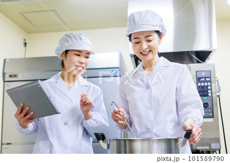 厨房でタブレットのレシピを確認しながら料理を作る白衣を着た女性調理員 厨房でタブレットのレシピを確認しながら料理を作る白衣を着た女性調理員 101589790