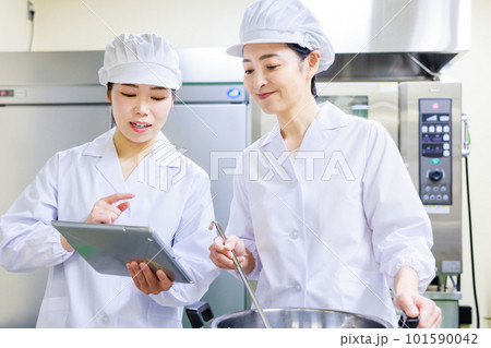 厨房でタブレットのレシピを確認しながら料理を作る白衣を着た女性調理員 厨房でタブレットのレシピを確認しながら料理を作る白衣を着た女性調理員 101590042