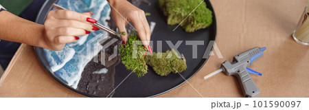 Close up of woman decorator making green ikebana on tray with epoxy resin in florist workshop 101590097