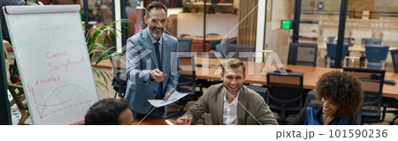 Mature business coach or speaker make flip chart presentation to diverse businesspeople at meeting Mature business coach or speaker make flip chart presentation to diverse businesspeople at meeting 101590236