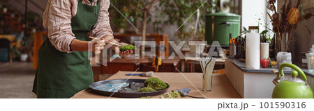 Professional woman decorator making green ikebana on tray with epoxy resin in florist workshop 101590316