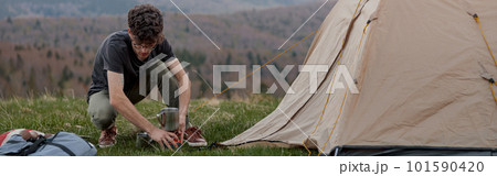 Caucasian young man setting tent on top of mountain. Beautiful view. Summer tourism. Caucasian young man setting tent on top of mountain. Beautiful view. Summer tourism. 101590420