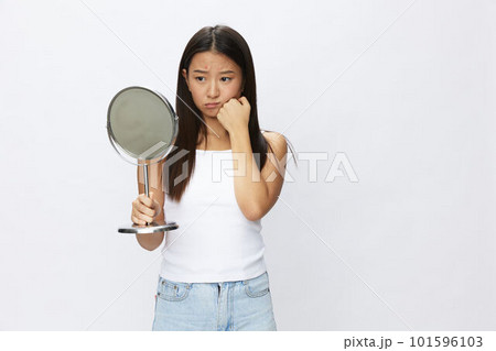 Asian woman with mirror in hand facial skin problems, acne and inflammation, red rash and allergies, chicken pox, sadness from rashes. Facial skin care concept for diseases and nerves 101596103