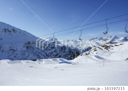 Ski lifts over snow covered land with mountains in background during sunny day, winter holiday travel concept 101597215