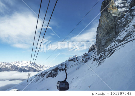 Gondola lift moving on cable over beautiful snowcapped Bernese mountain under cloudy sky at ski resort in Jungfrau, Switzerland, winter holiday and nature concept 101597342