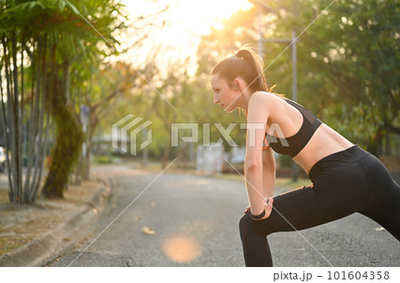 Active fitness caucasian woman warming up before exercises in the park with bright sunlight on background 101604358