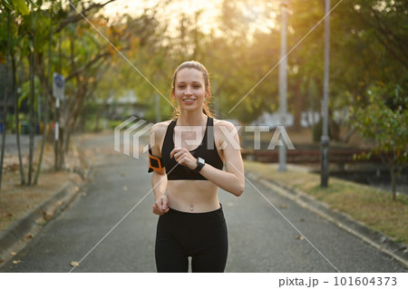 Delighted athletic woman in sportswear jogging in public park. Healthy lifestyle, sport, wellness concept 101604373