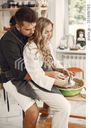 Mutual creative work. Young beautiful couple in casual clothes and aprons. People creating a bowl on a pottery wheel in a clay studio. Mutual creative work. Young beautiful couple in casual clothes and aprons. People creating a bowl on a pottery wheel in a clay studio. 101606763