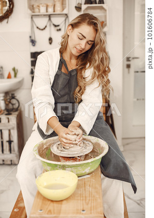 Female potter working with clay on wheel in studio. Clay with water splattered around the potter wheel. 101606784