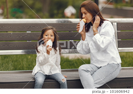 Family in a city. Little girl eats ice cream. Mother with daughter sitting on a bench. 101606942