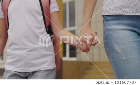 mother holds happy daughter by the hand, accompany little child with backpack to school, study in preschool preparation, walk through schoolyard, first grade student with school bag on his shoulders 101607707