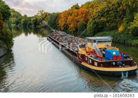 Transportation industry. Ship barge transports scrap metal and sand with gravel. Barge loaded with scrap metal is on the roadstead. Scrap metal transportation by water. Barge laden by metal salvage 101609263
