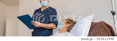 Doctor in mask writing down patient symptoms in hospital ward during Covid-19 epidemic 101611446