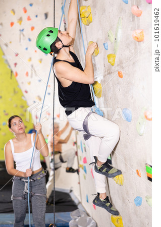 young positive man, insured by trainer, moving up artificial climbing wall indoors young positive man, insured by trainer, moving up artificial climbing wall indoors 101619462