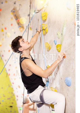 young positive man, insured by trainer, moving up artificial climbing wall indoors young positive man, insured by trainer, moving up artificial climbing wall indoors 101619465