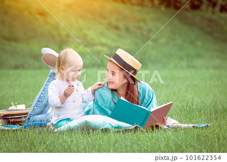 Mother is reading book for baby girl lying on the grass in the park Mother is reading book for baby girl lying on the grass in the park 101622354