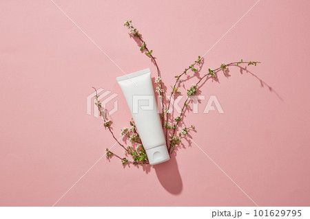 White empty plastic tube with facial moisturizer cream or facial cleanser and small branches flower on pink background. Mockup for presentation of cosmetic products. Top view, flat lay. 101629795